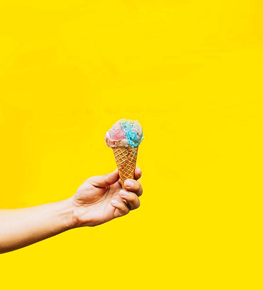 Hand holding ice cream cone on yellow background. Hand holding a waffle cone ice cream isolated. Waffle cone ice cream concept on yellow background