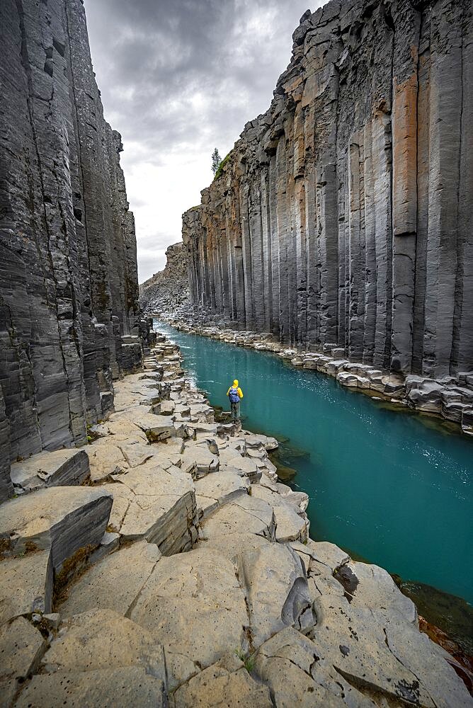 Tourist standing by the river in Stuolagil Canyon, turquoise blue river between basalt columns, Egilsstadir, Iceland, Europe