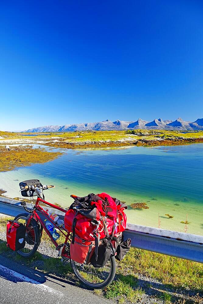 Packed touring bike, crystal clear water in a shallow bay, view of the mountain range Seven Sisters, cycle tourism, cycle trip, Heroey Island FV 17, Kystriksveien, Nordland, Norway, Europe