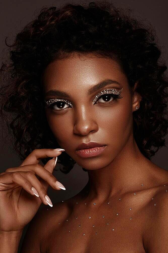 Beautiful African American woman with trendy makeup, rhinestones on her eyes and curly hair. Beauty face. Photo taken in the studio