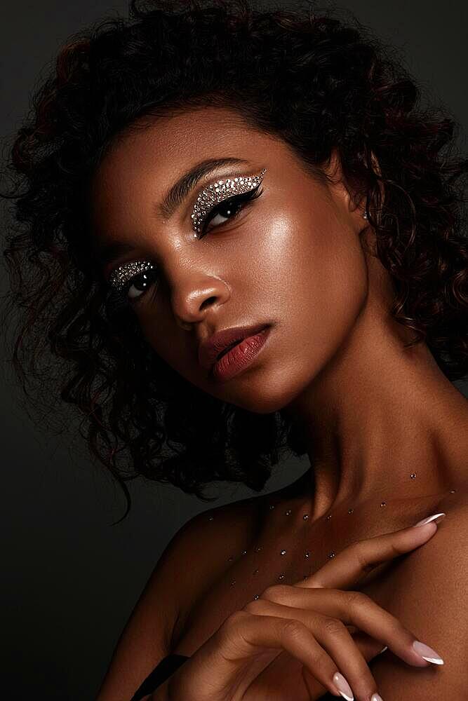 Beautiful African American woman with trendy makeup, rhinestones on her eyes and curly hair. Beauty face. Photo taken in the studio