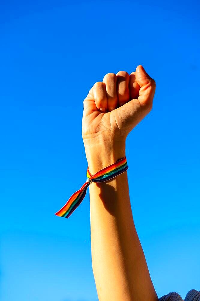 Hand of a woman with closed fist in favor of feminism, blue sky background, fighting in favor of women, Female strength, LGTB flag