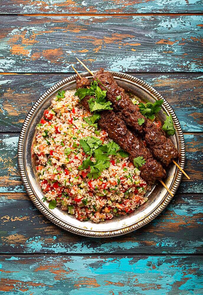 Middle eastern Turkish dinner with meat kebab and couscous salad tabbouleh on rustic metal plate on wooden background top view, traditional Arab meal