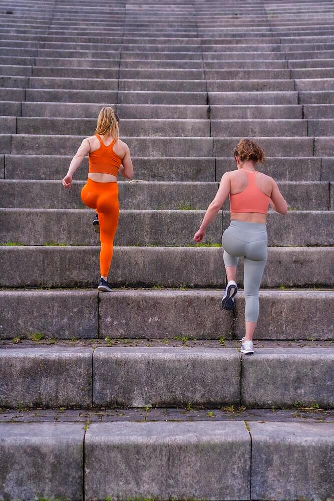 Two young fitness woman in a city park, running up the big steps