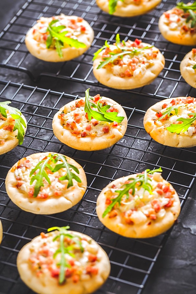 Small tarte flambee or mini pizza with onion, bacon and arugula on black background