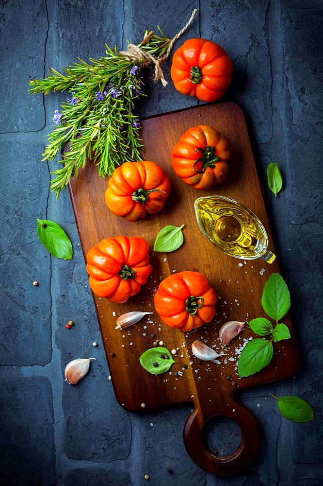 Italian cuisine - Olive oil, tomato and herbs on rustic cutting board