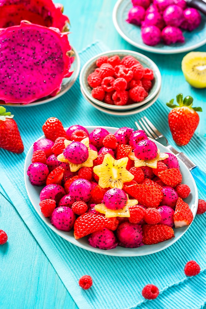 Fresh dragon fruit salad with strawberries, rspberries and start fruit (carambola) on cyan background