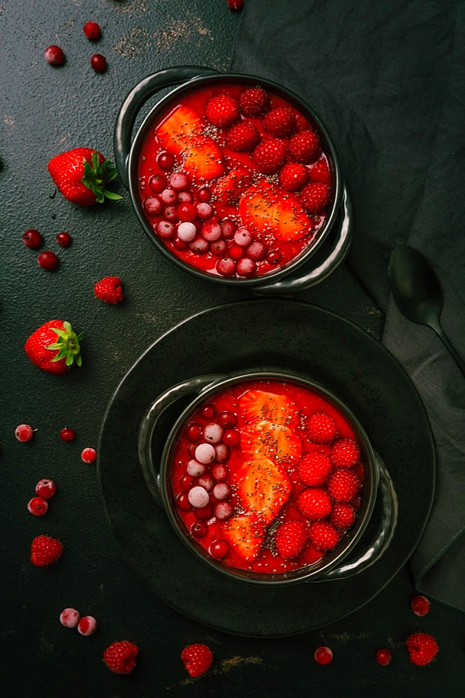 Breakfast red smoothie bowl with chia seeds, strawberry, raspberry and redcurrants on black background