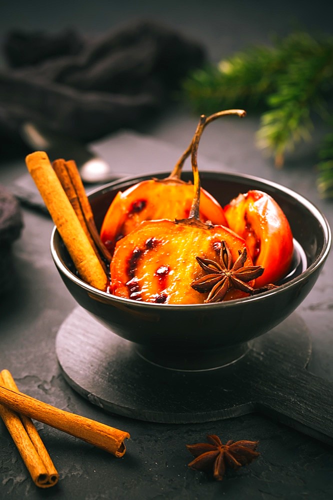 Christmas dessert - flamed tamarillo in hot wine punch with cinnamon and anise on black background