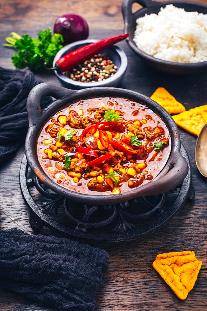 Bowl of chili con carne with rice and toppings on wooden table