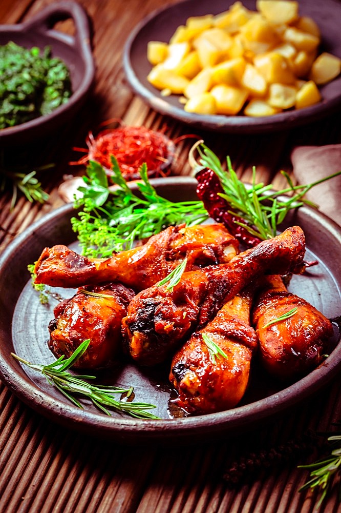 Marinated chicken drumsticks with baked potatoes and spinach on wooden background