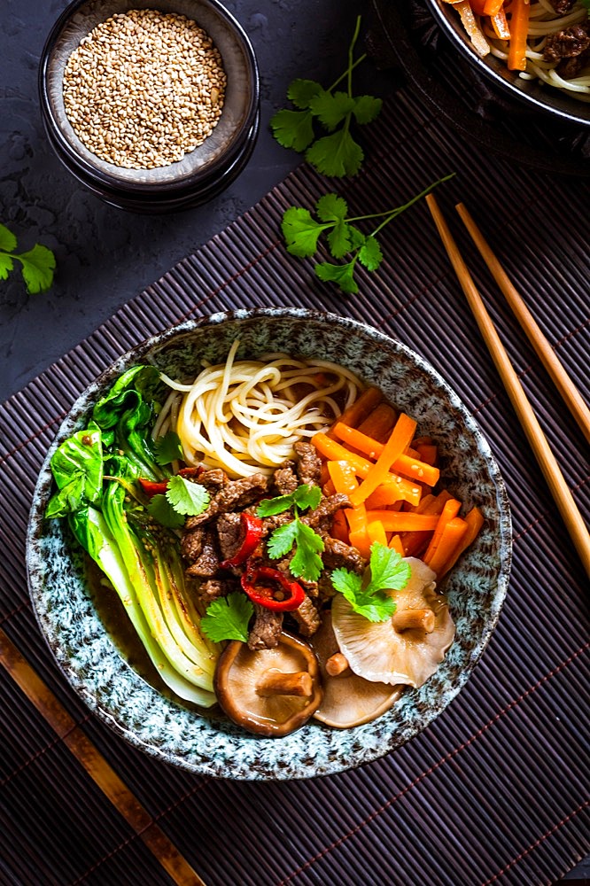 Asia style ramen soup with udon noodle, beef, shiitake, pak choi cabbage and carrots on black background