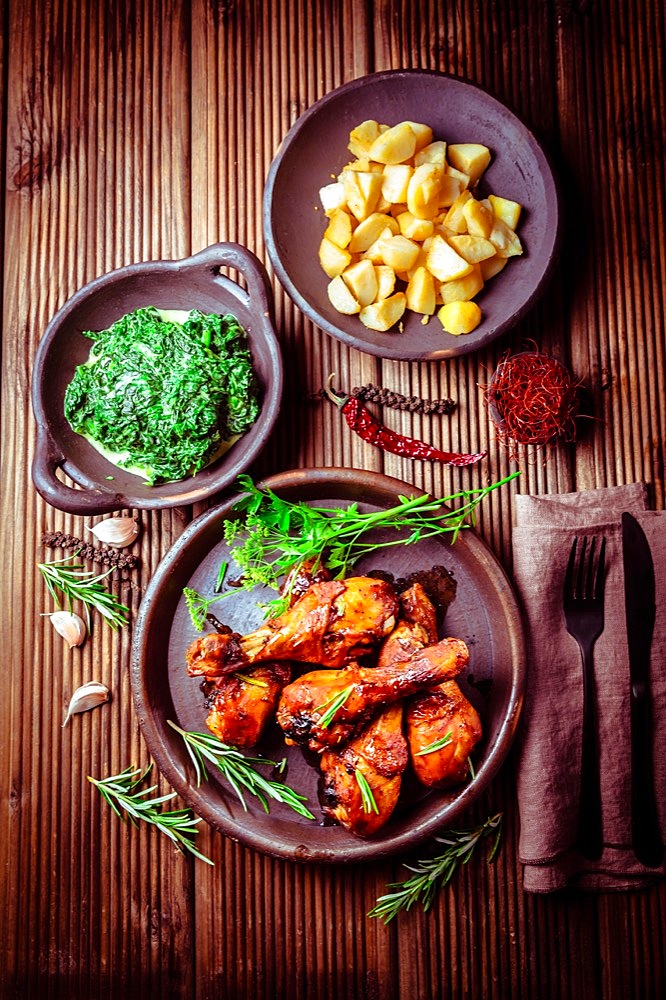 Marinated chicken drumsticks with baked potatoes and spinach on wooden background