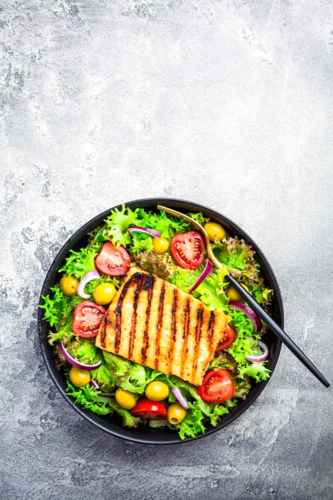 Fresh salad with grilled cheese, tomatoes and olives on grey