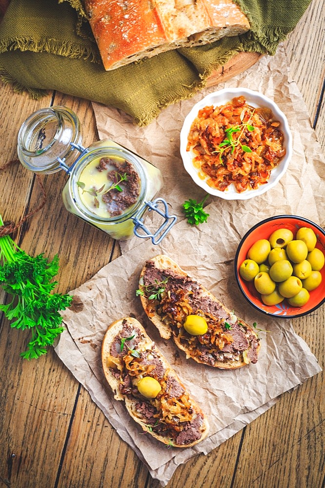 Fresh homemade chicken liver pate on ciabatta bread with roasted onions and olives on wooden table