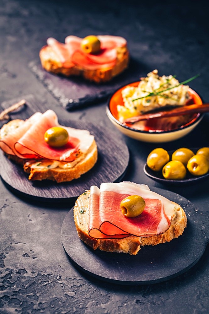 Roasted bread or open sandwich with garlic butter spread and serano ham and olive on dark background