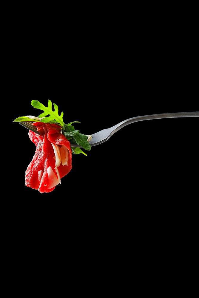 Slice of marbled beef carpaccio on fork over black background