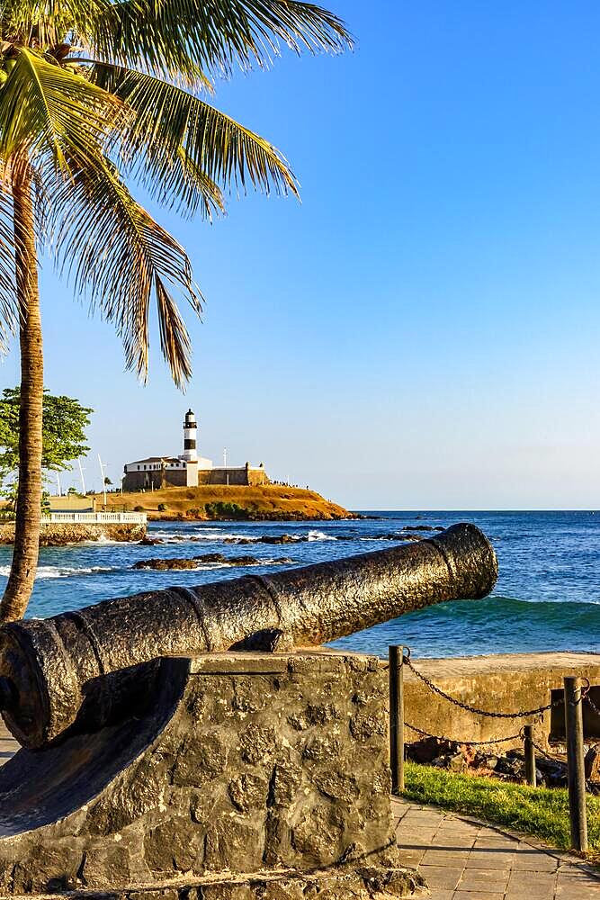 Old cannon from the time of the empire used in the defense of the city of Salvador in Bahia, with Farol da Barra and the sea in the background, Brasil