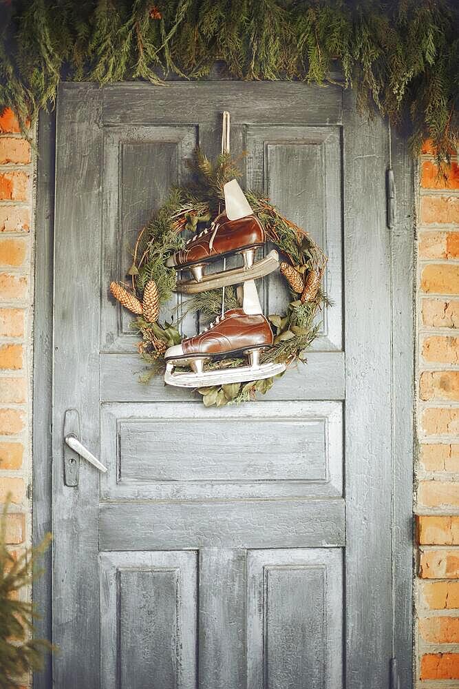 Beautiful Christmas composition: part of a vintage house, old brick wall, street decor, blue gray door with a Christmas wreath and vintage skates