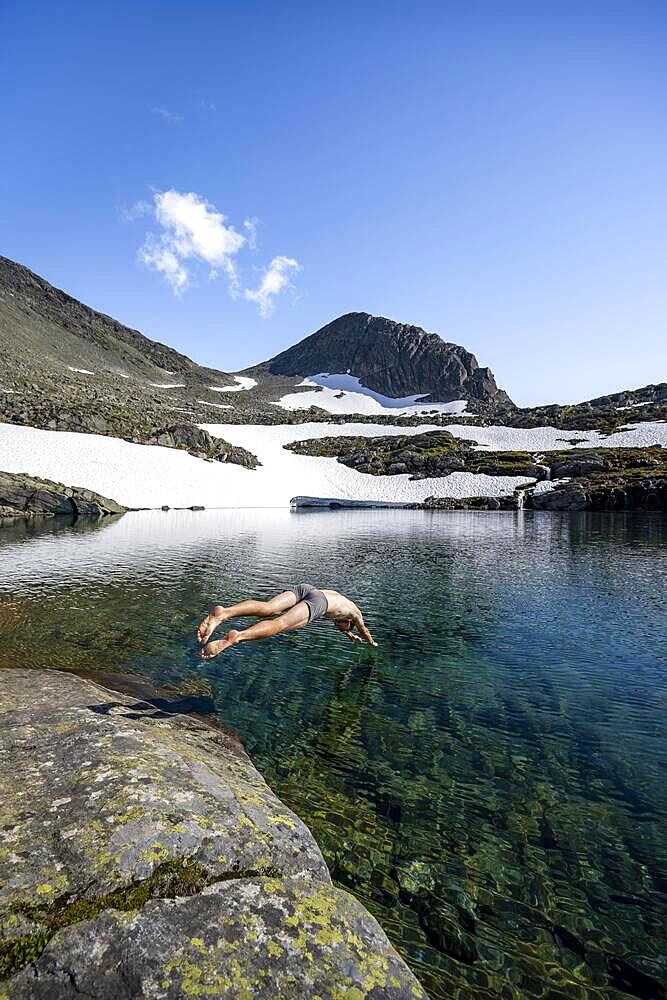 Young man jumps into a mountain lake, Skalavatnet, ascent to the summit of Skala, Norway, Europe