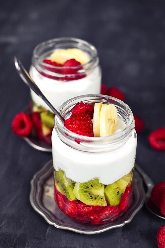 Healthy fruit snack with raw raspberry and kiwis and yoghurt layered in glass on dark background