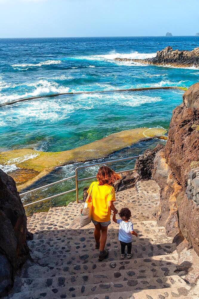 A mother with her son going down into the La Maceta rock pool on the island of El Hierro in the Canary Islands