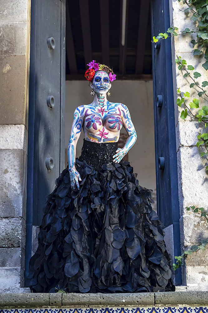 A gorgeous Hispanic Brunette model poses with traditional skull sugar makeup paint for a Mexican festival