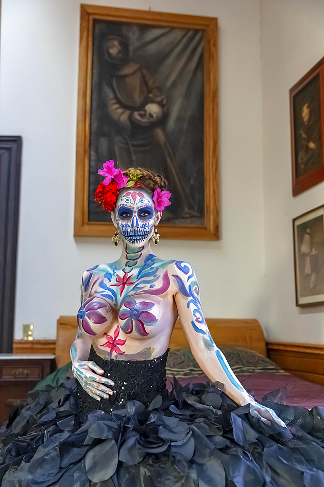 A gorgeous Hispanic Brunette model poses with traditional skull sugar makeup paint for a Mexican festival