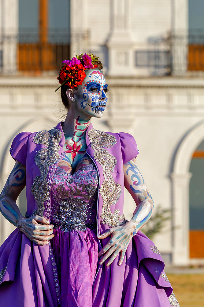 A gorgeous Hispanic Brunette model poses with traditional skull sugar makeup paint for a Mexican festival