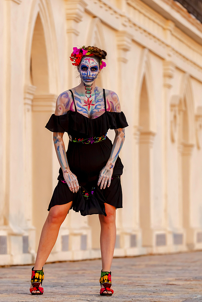 A gorgeous Hispanic Brunette model poses with traditional skull sugar makeup paint for a Mexican festival