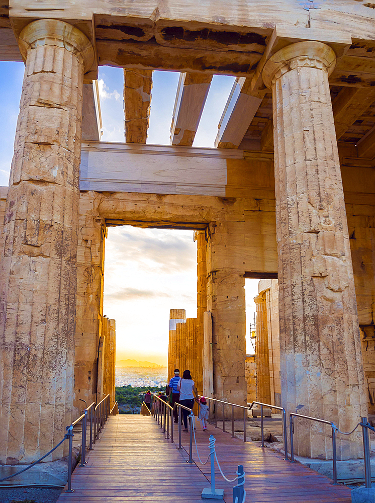 Columns of Propylaea entrance gateway of Acropolis, Athens, Greece overlooking the sunset and city and tourists leaving the famous ancient complex