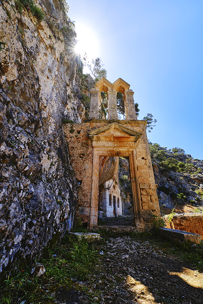 Ruins of abandoned Orthodox Katholiko monastery near Gouverneto moni in Avlaki gorge, Akrotiri peninsula, Chania, Crete, Greece. Ruins of entrance gate to the area. Upshot against sun. Spring daytime