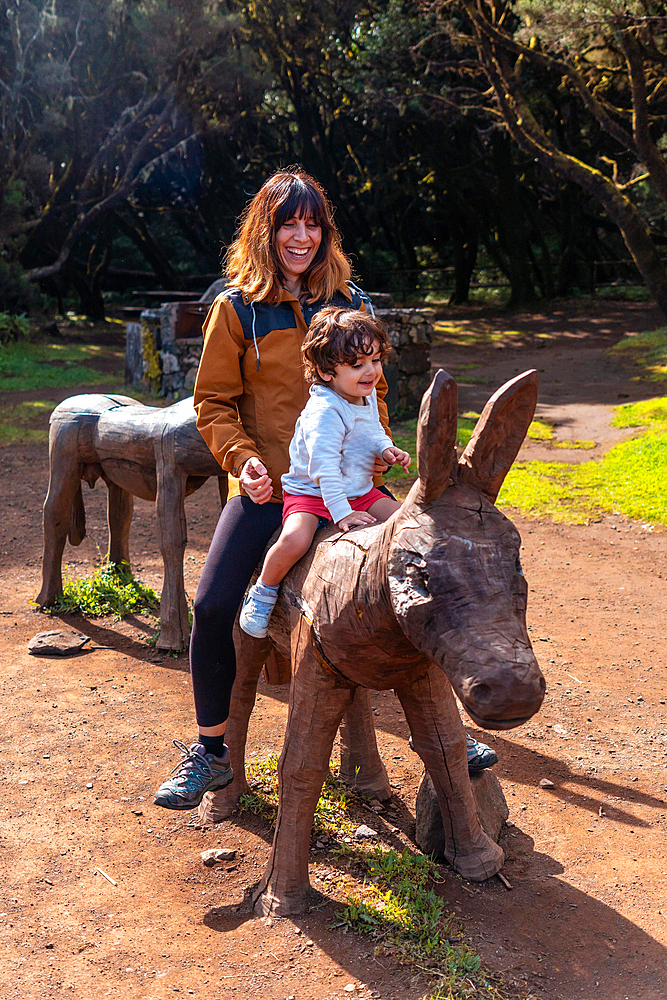 A boy and a mother playing on the wooden horse in the leisure area at Laguna Grande in the Garajonay natural park on La Gomera, Canary Islands