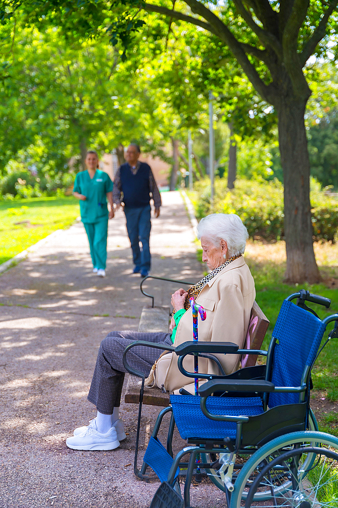 Portrait of an elderly woman sitting on a chair in the garden of a nursing home in a wheelchair