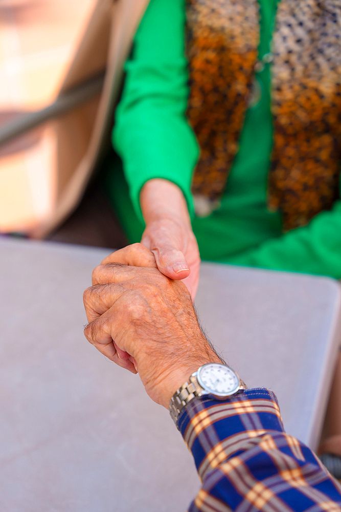 Detail of the hands of two elderly people in the garden of a nursing home or retirement home holding hands in a moment of affection