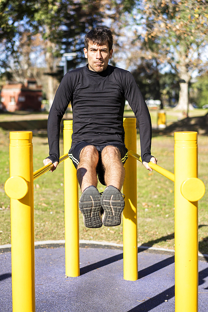 Frotn view of a young man doing abdominal exercises on a public equipment in outdoor fitness