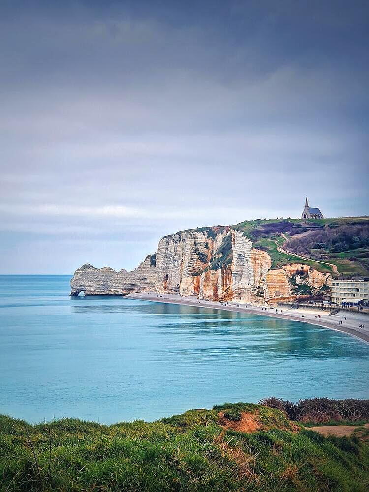 Idyllic view to Etretat coastline with the famous Notre-Dame de la Garde chapel on the Amont cliff. Shore washed by Atlantic ocean waters, Normandy, France, Europe