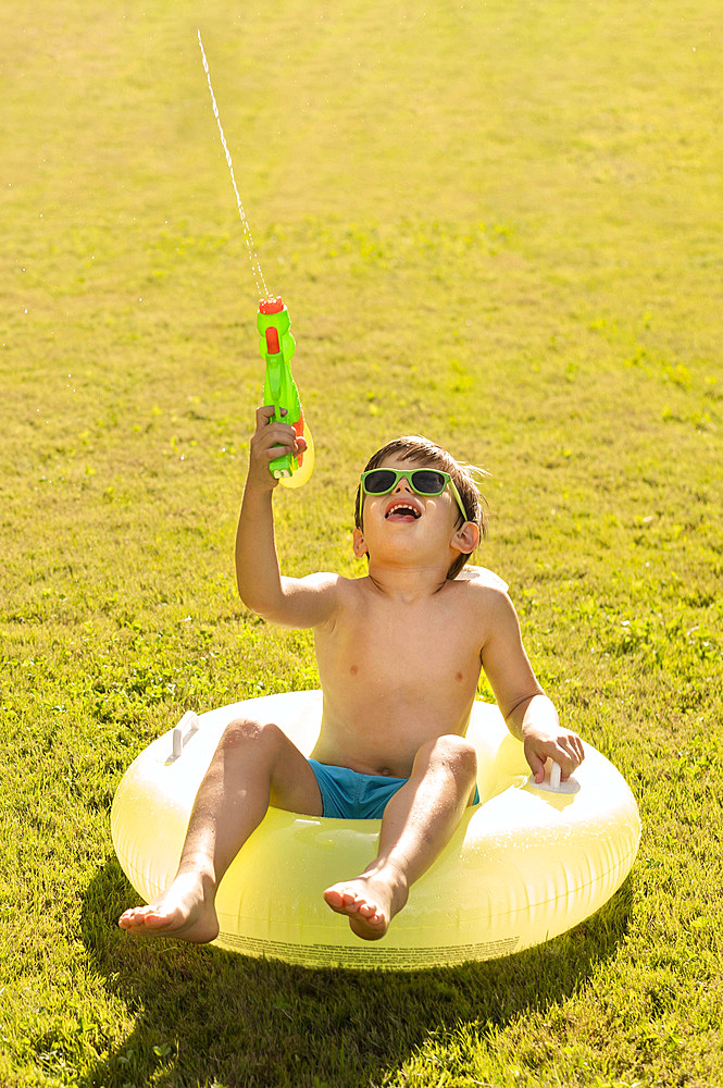 Boy with hat sunglasses playing with water gun