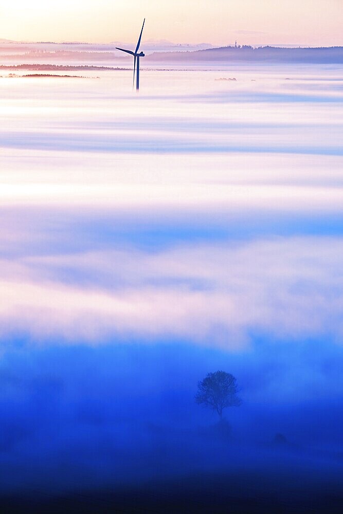 Scenic view at a wind turbine rising out of the morning fog in a rural landscape in autumn