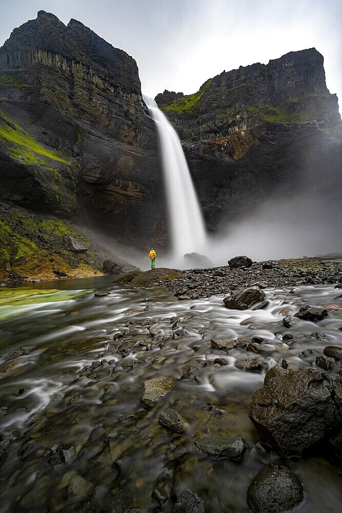 Young man with yellow jacket standing in front of waterfall, Haifoss and Granni waterfall at a canyon, Fossá í Þjórsárdal, with river í Þjórsárdal, long exposure, dramatic landscape, Hekla, Iceland, Europe