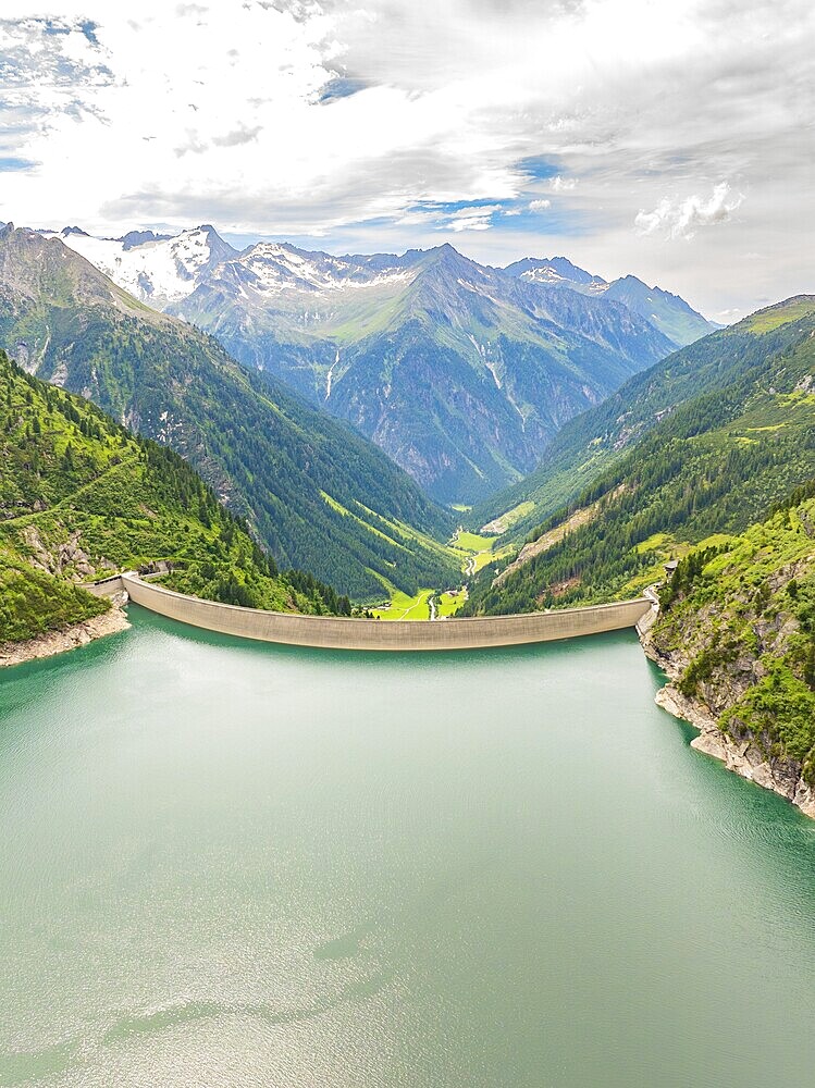 A large reservoir with a dam, surrounded by high mountains and green vegetation under a partly cloudy sky, Klein Tibet, Zillertal, Austria, Europe