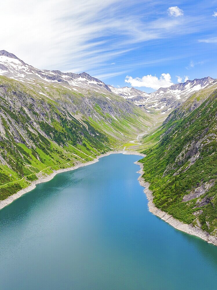 Mountain landscape with an elongated lake in the centre, surrounded by green hills and snow-capped mountains under a blue sky, Klein Tibet, Zillertal, Austria, Europe