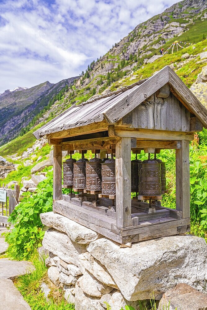 Traditional wooden prayer wheels stand on a stone foundation in the midst of an impressive mountain landscape, Little Tibet, Zillertal, Austria, Europe