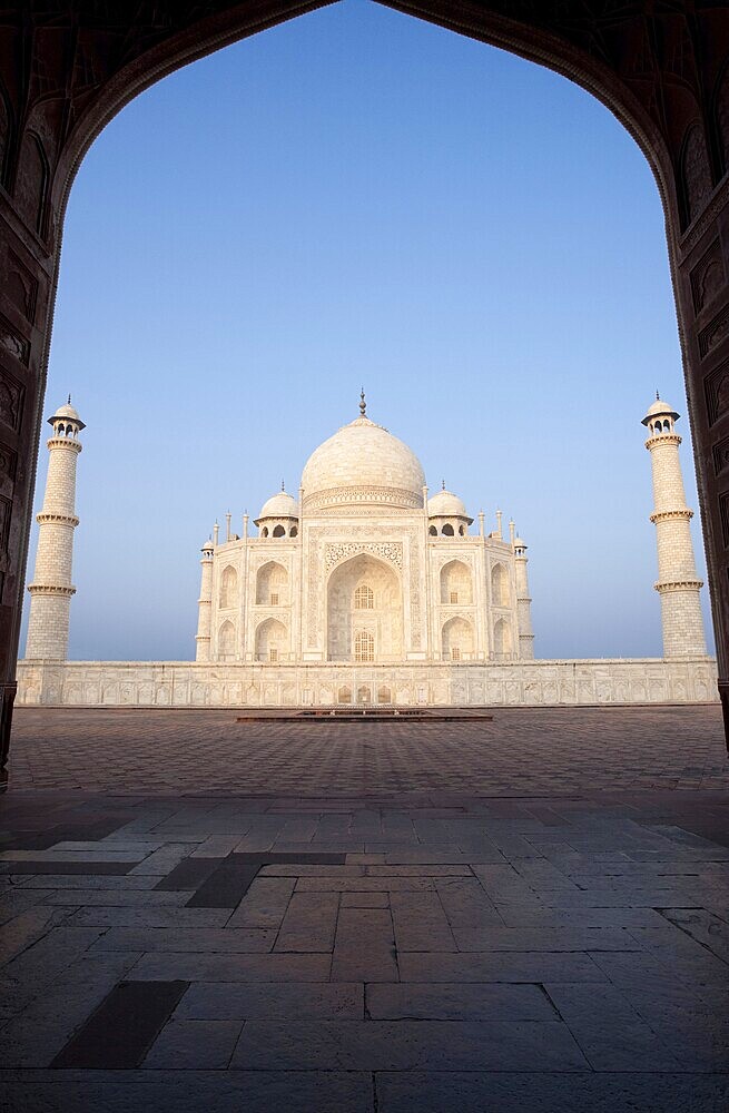 The beautiful marble of the Taj Mahal shines brightly seen through the east jawab's large gateway at a time when no people are present