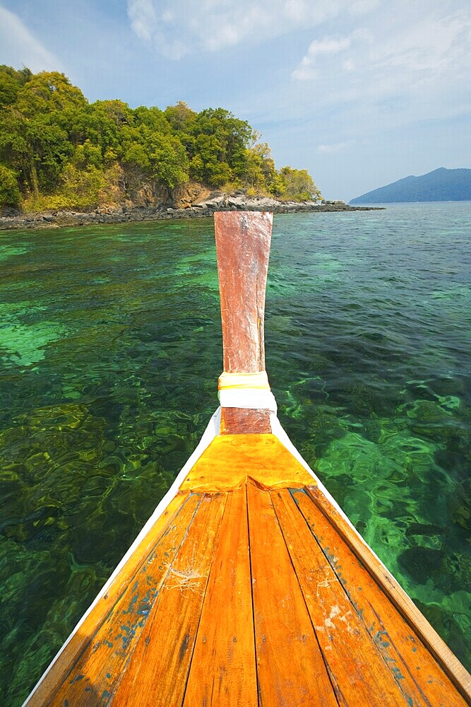 The bow of a traditional longtail boat overlooks the crystal clear water and coral reef in Tarutao national park, Thailand, an area known for great diving and snorkeling, Asia