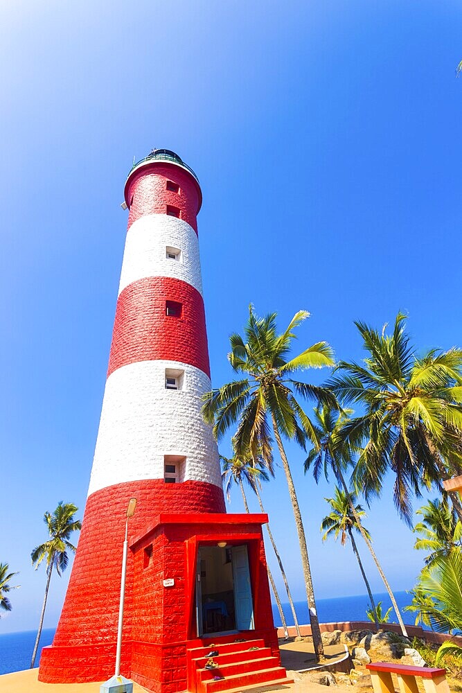 Ocean and horizon seen behind red and white striped lighthouse at Kovalem Beach, Kerala, India on a clear, blue sky day