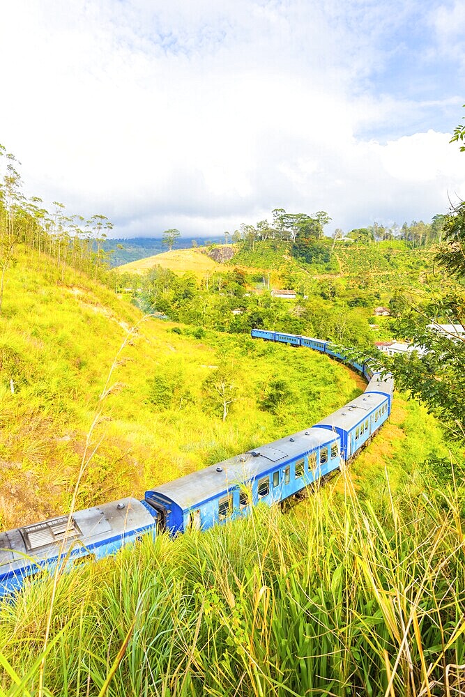 Passenger train moving away on unique circular curving portion of spiral track around a hill in order to gain elevation, Demodara Loop, at Demodara Railway Station in hill country of Sri Lanka