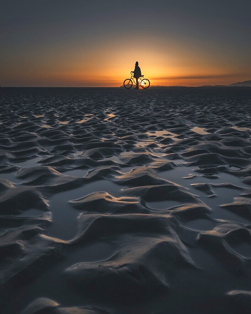 Silhouette of a person with a bicycle on a beach during a picturesque sunset, Tofino, BC, Canada, North America