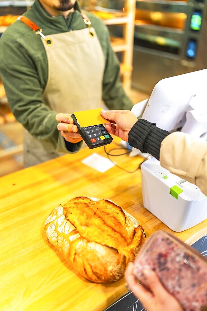 Vertical cropped photo of the hands of a woman paying using credit card in a modern bakery