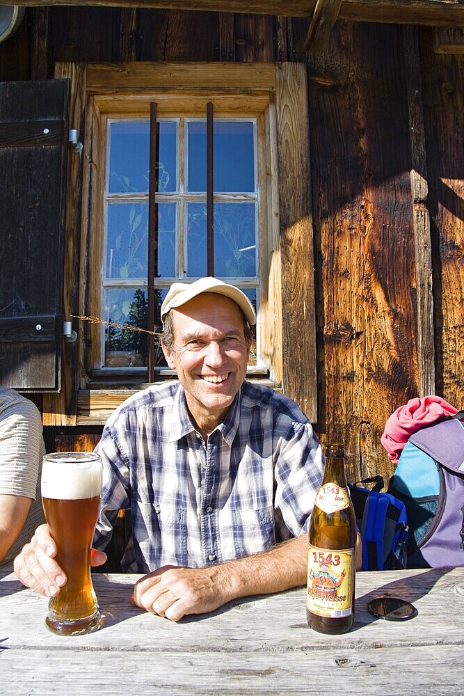 Husband drinking wheat beer, having a break from a mountain hike, mountain pasture, Mitterhuettet cabin, Alps, Germany, Europe